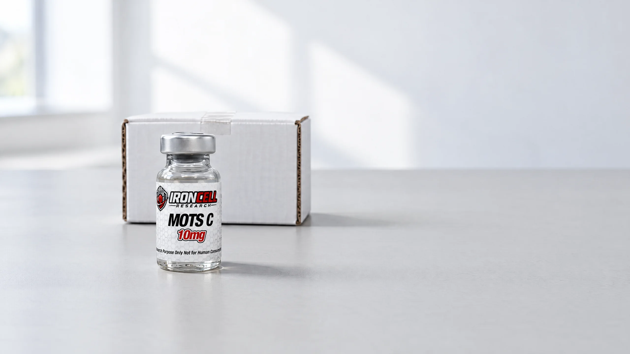 IronCell Research MOTS C 10mg vial in front of a closed white shipping box on a light grey desk